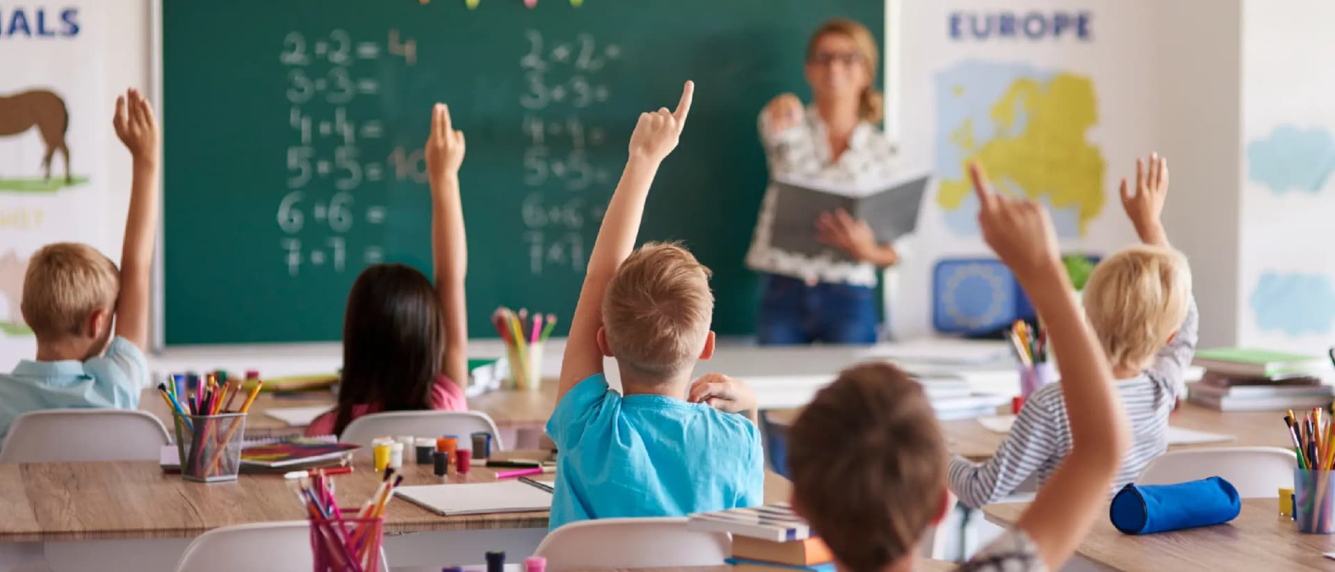 Children raising hands in classroom during math lesson