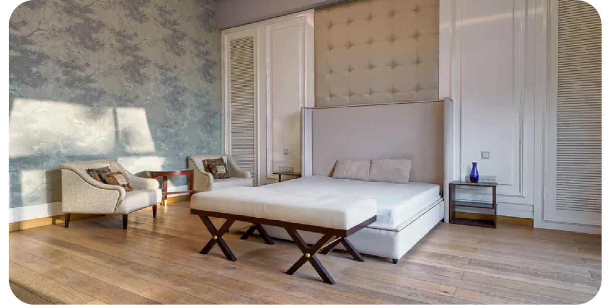 Sunlit bedroom with a bed and two armchairs