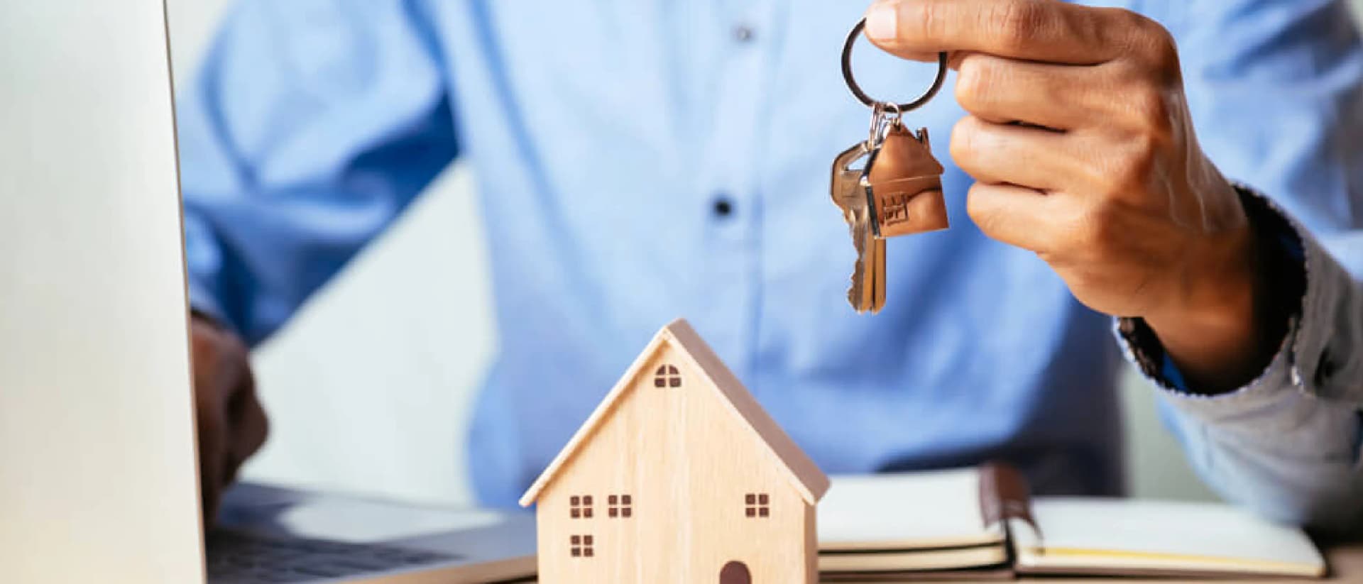 A hand holding keys with a house keychain and model