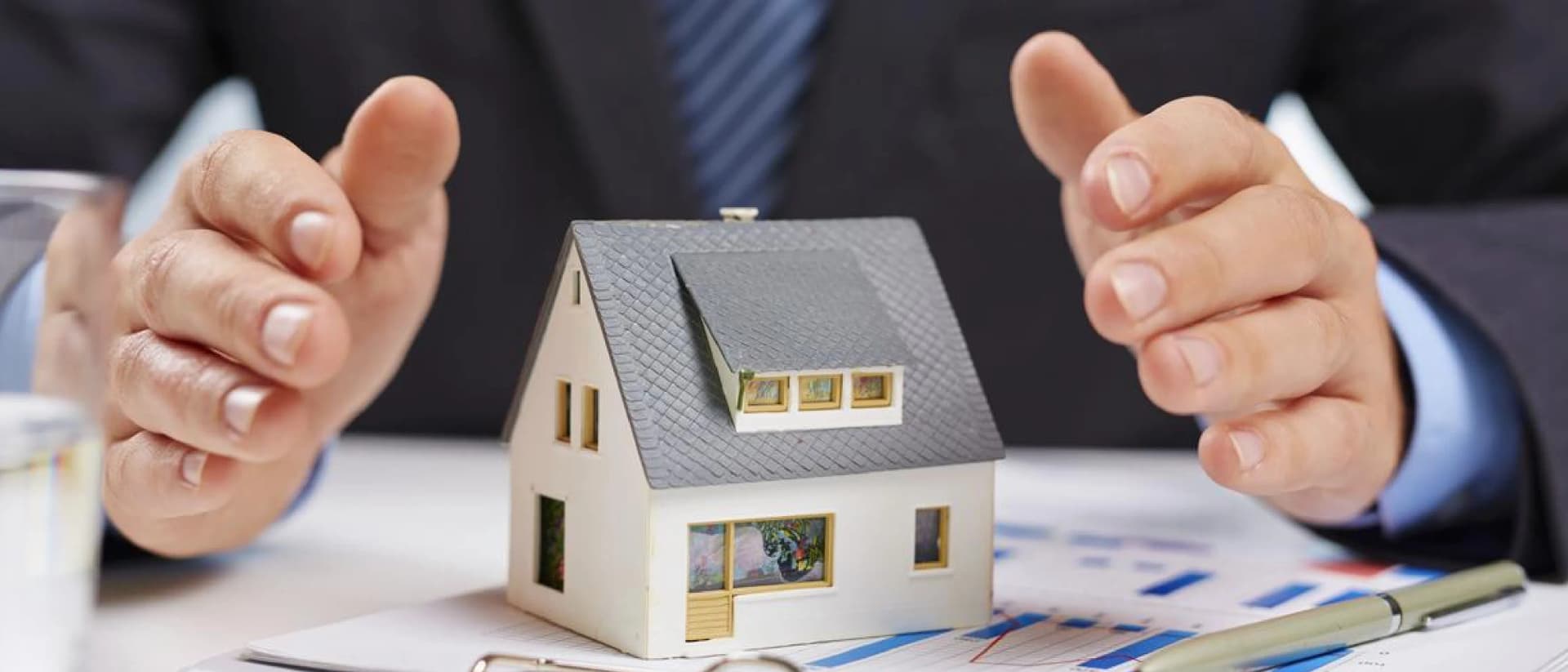Hands protect a small house model on a desk