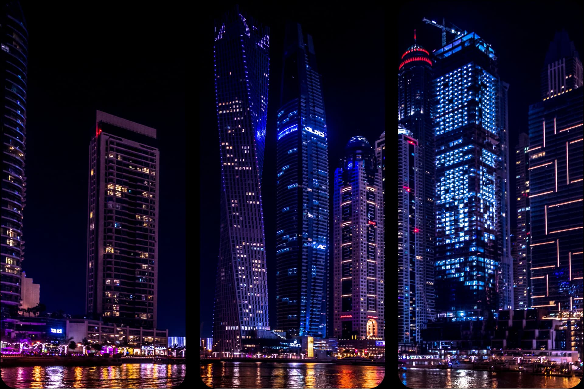 Night view of illuminated skyscrapers reflecting on water.