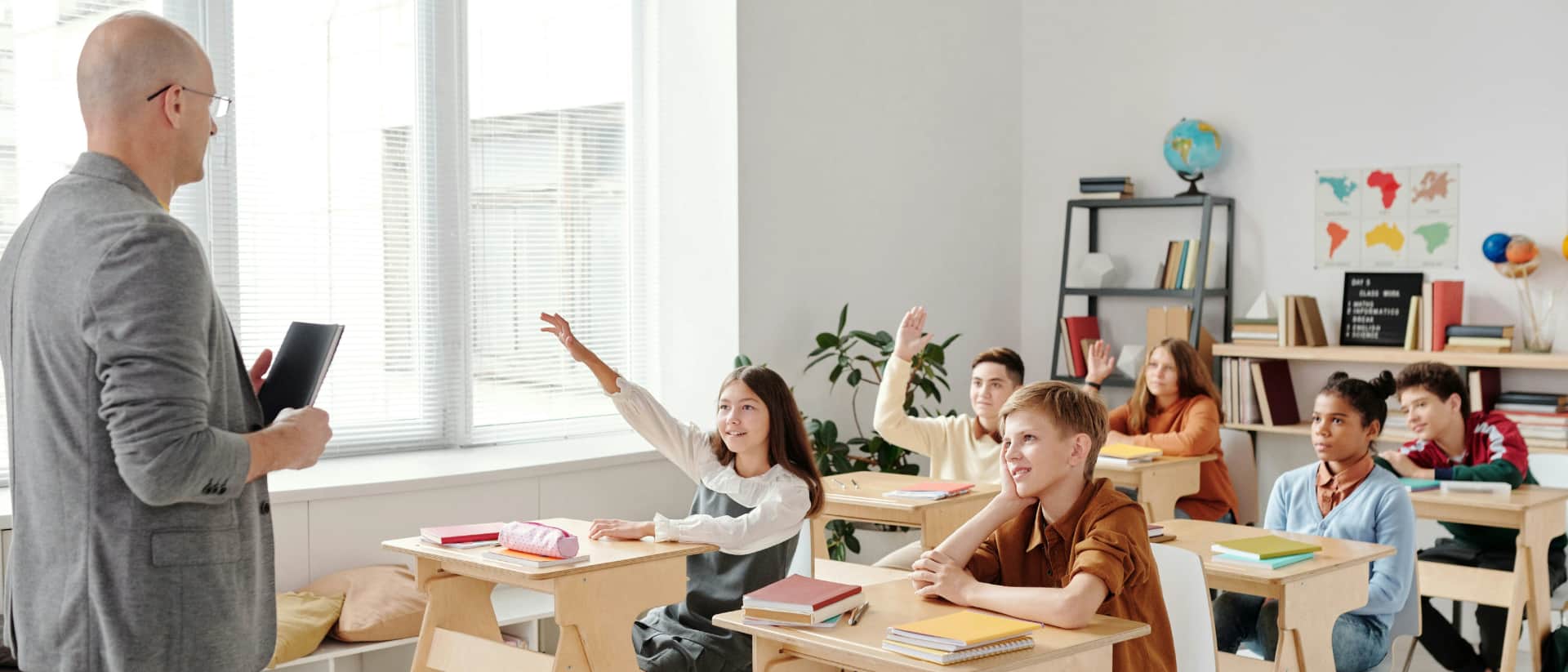 A teacher faces students with raised hands in a classroom