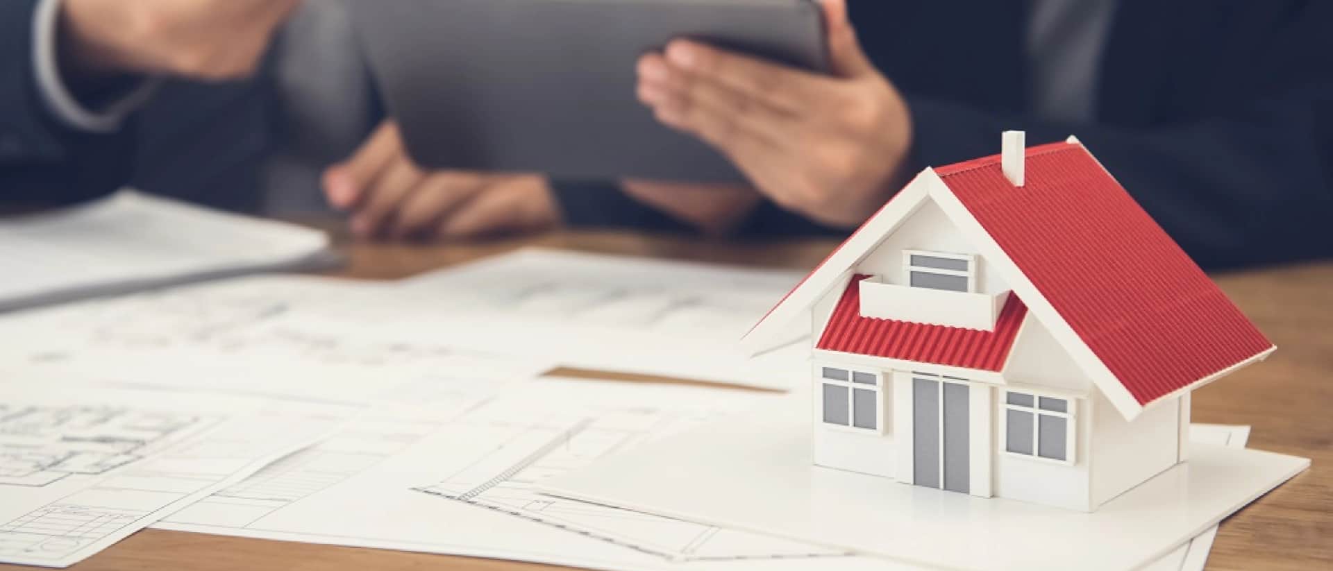 Small house model on blueprints, person with tablet