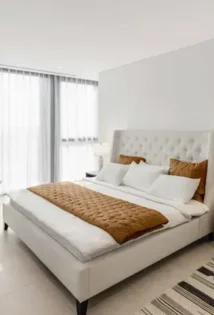 A bright and airy bedroom with a white bed and a brown blanket.