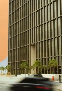 Car driving on a street in front of a tall skyscraper with a glass facade.