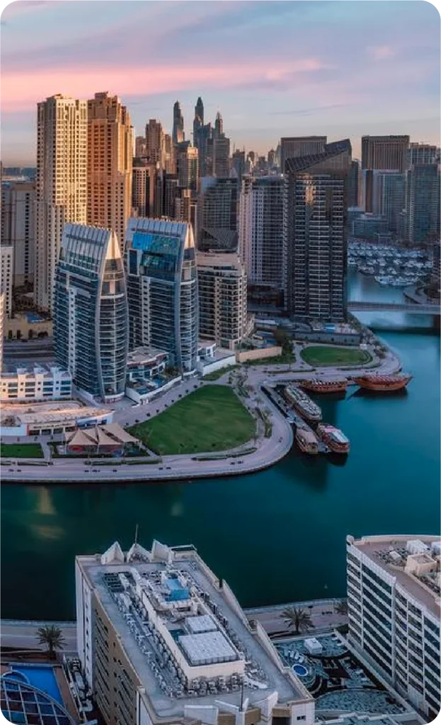 Aerial view of Dubai Marina with waterfront buildings, green spaces, and marina waters at sunset.