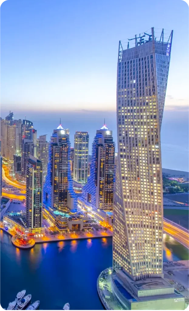 Dubai Marina skyline with the iconic Cayan Tower and illuminated buildings at dusk.