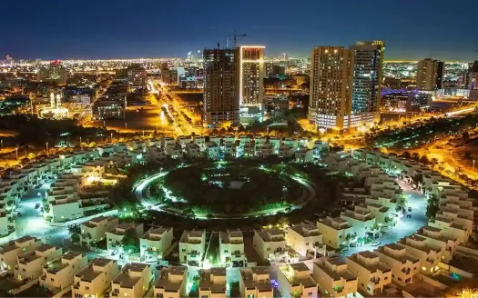 Night view of Jumeirah Village Circle with illuminated circular residential layout and city skyline.