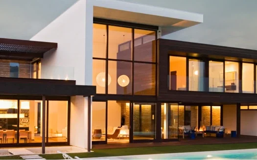 Modern luxury villa with large glass windows and a pool at sunset.