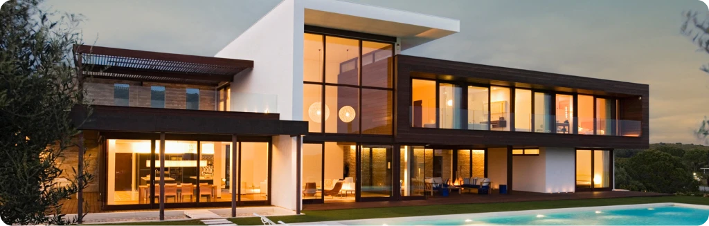 Modern luxury villa with large glass windows and a pool at sunset.